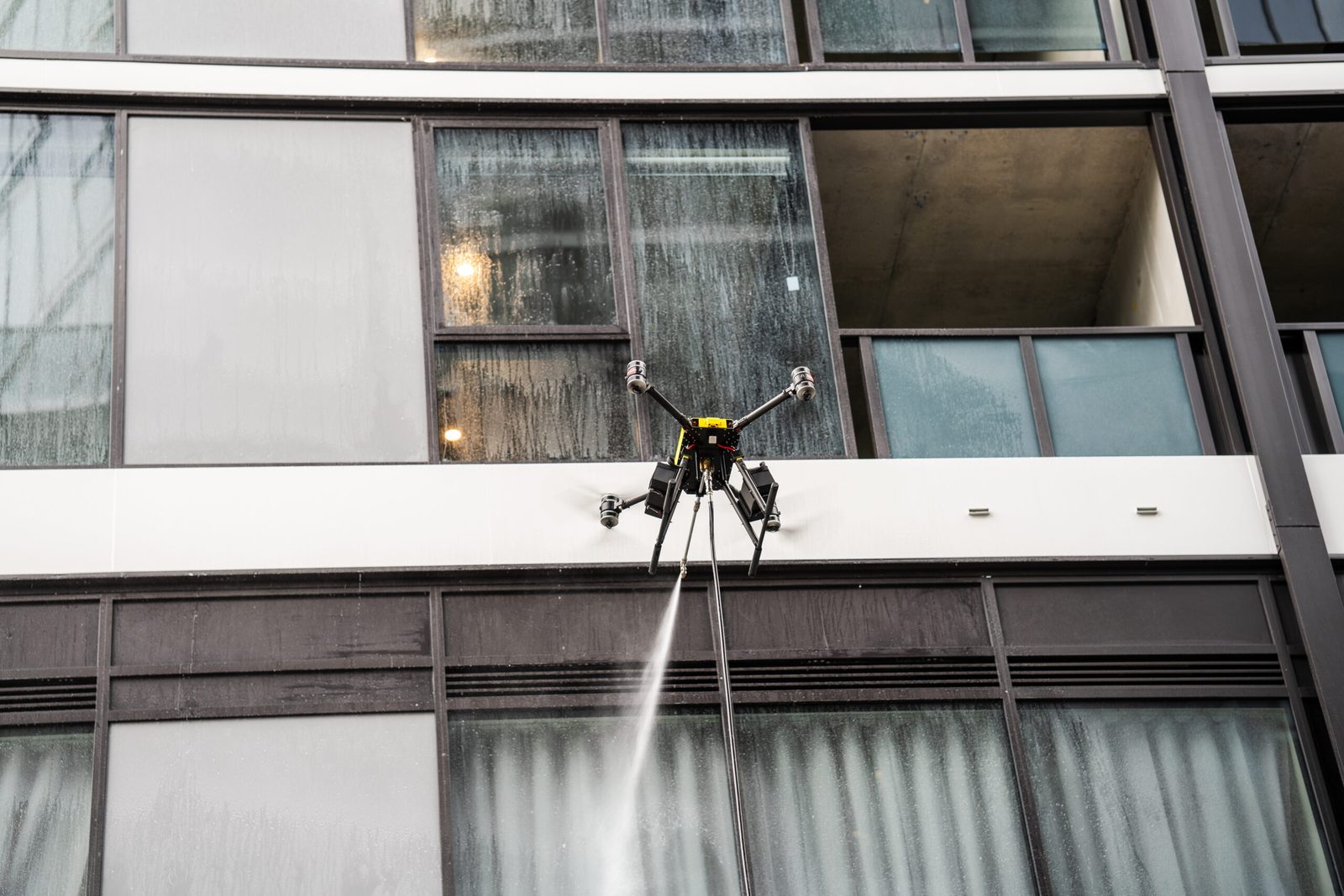 Drone rinsing a glazed curtain wall elevation on a commercial building